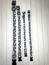 Load image into Gallery viewer, A visual comparison of Dave the Sheep collars in different sizes. Light grey dog collars with white and black sheep print on, black hardware and silver d ring. Lunapalooza logo on one end. Showing sizes puppy, small, medium, large and extra large.